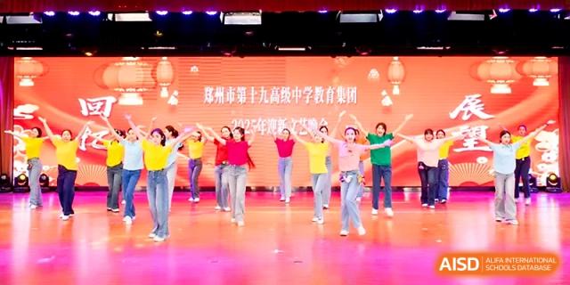 Students in colorful t-shirts perform a synchronized dance routine on a brightly lit stage during a festival at Zhengzhou No.19 High School.