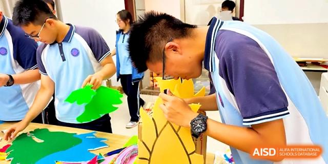 A student focuses intently on crafting a large yellow dragon head decoration for a cultural event at Zhengzhou No.19 High School.
