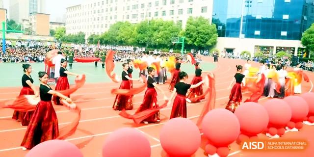 A large group of students in red costumes perform a choreographed dance on the school's outdoor athletic field at Zhengzhou No.19 High School.