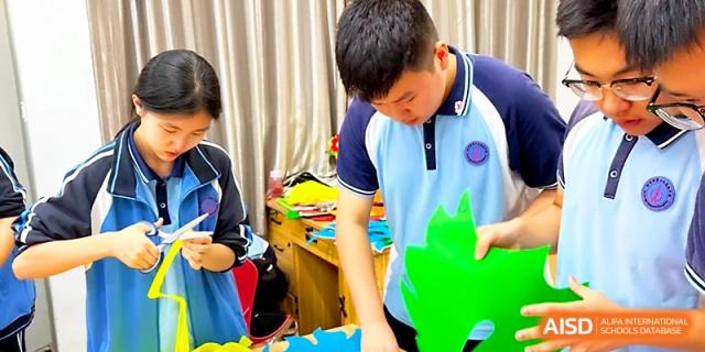 Students in blue and white school uniforms work together to cut out green paper decorations for a project at Zhengzhou No.19 High School.