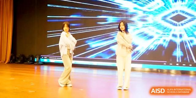 Two students in modern white outfits perform a contemporary dance routine on stage with a digital backdrop at Zhengzhou No.19 High School.