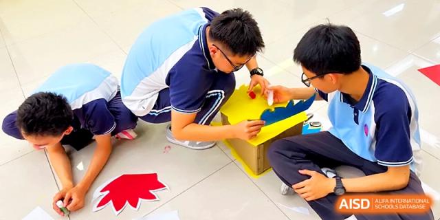 A group of students collaborate on the floor to assemble a large, colorful dragon prop for a parade at Zhengzhou No.19 High School.