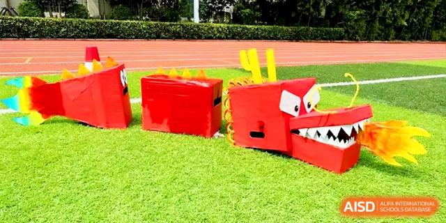 Large red cardboard dragon props sit on the green grass of the athletic field, ready for a performance at Zhengzhou No.19 High School.