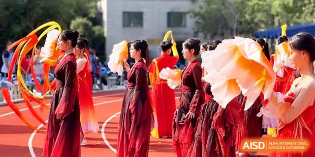 Performers wearing deep red traditional dresses stand in line with large decorative fans on the running track at Zhengzhou No.19 High School.