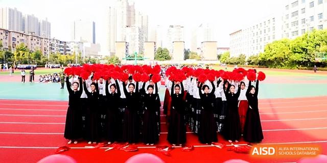 A large formation of students in dark uniforms raises red props in unison during a massive field performance at Zhengzhou No.19 High School.