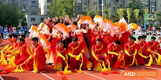 A troupe of dancers in bright red and yellow costumes performs a high-energy routine on the outdoor track at Zhengzhou No.19 High School.