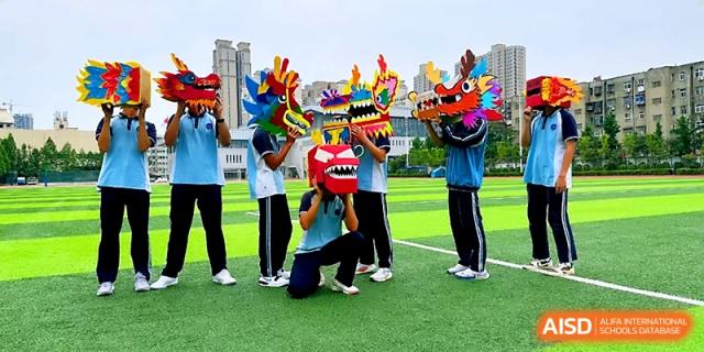 Students on the green sports field pose with various colorful dragon masks they have created for a festival at Zhengzhou No.19 High School.