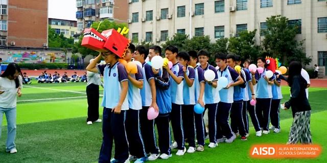 Students in blue uniforms line up on the school field, with the front student wearing a red dragon head mask at Zhengzhou No.19 High School.
