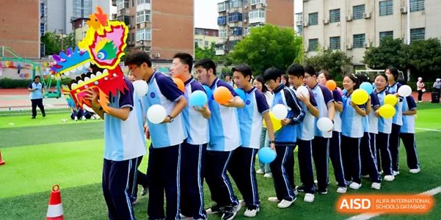 A row of students in matching blue school polo shirts hold colorful balloons during a sports day event at Zhengzhou No.19 High School.