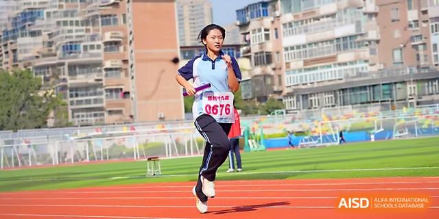 A female student athlete in a blue and white tracksuit runs a race on the red track during a sports meet at Zhengzhou No.19 High School.