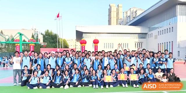 A large group of students in blue tracksuits pose for a formal group photo in front of the school building at Zhengzhou No.19 High School.