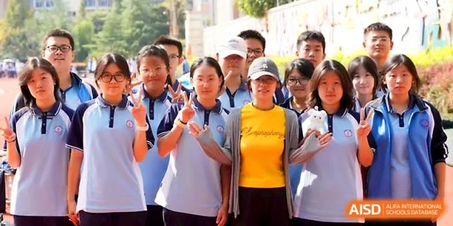 A group of students and a teacher in a yellow shirt smile and make peace signs during an outdoor school event at Zhengzhou No.19 High School.