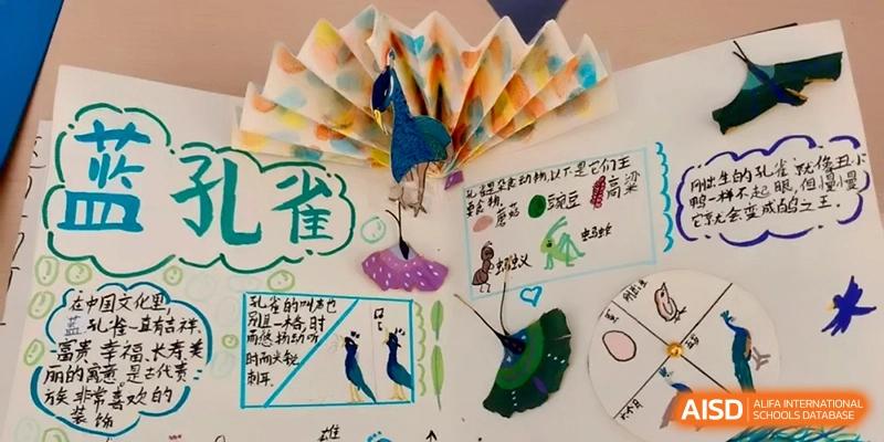 Close-up of a colorful student art project featuring a paper peacock and hand-drawn illustrations on a display board at Beijing Financial Street Runze School.