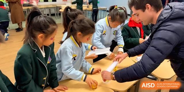 Groups of students collaborate at wooden tables on a hands-on building project using white paper tubes and tools at Beijing Financial Street Runze School.