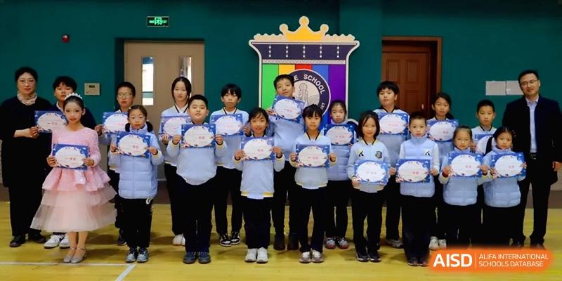 A group of elementary students stand proudly in a row holding certificates in front of a colorful school banner at Beijing Financial Street Runze School.