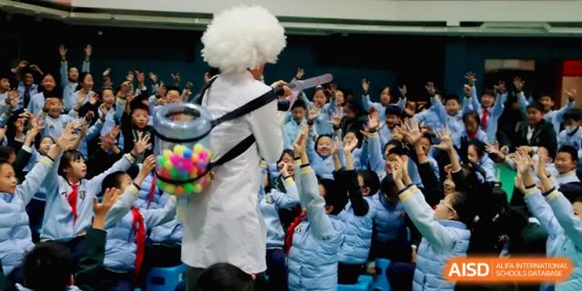A performer in a white lab coat and wig interacting with a crowd of excited students at Beijing Financial Street Runze School.