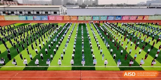 A large group of students in uniform performing synchronized exercises on the green field at Beijing Financial Street Runze School.