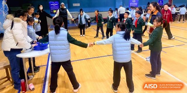 Students in blue vests participate in a group dance or team-building activity indoors at Beijing Financial Street Runze School.