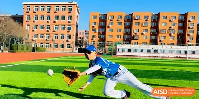 A student athlete in a baseball uniform catches a ball on the green turf at Beijing Financial Street Runze School.