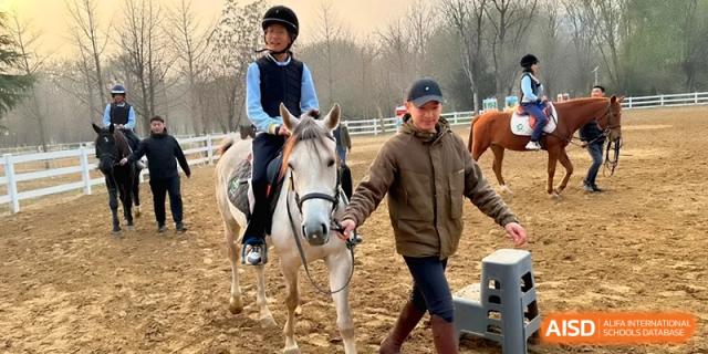 A young student rides a white pony guided by an instructor during an equestrian lesson at Beijing Financial Street Runze School.