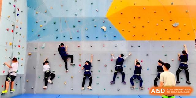 Four students practice their climbing skills on a colorful indoor rock-climbing wall at Beijing Financial Street Runze School.