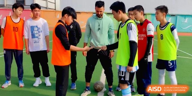 A soccer coach talks to students on the field during a team practice session at Beijing Financial Street Runze School.