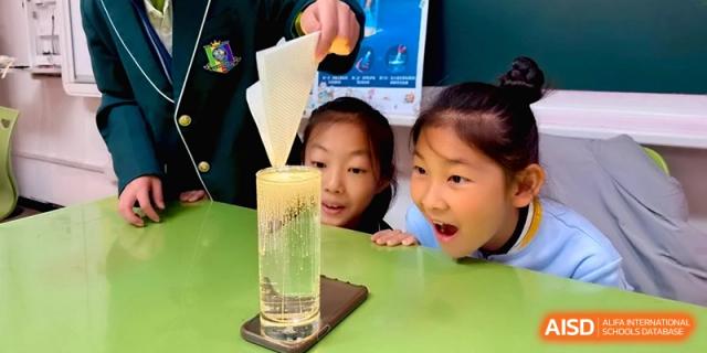 Two young girls look curiously at a tall glass during a health and nutrition lesson at Beijing Financial Street Runze School.