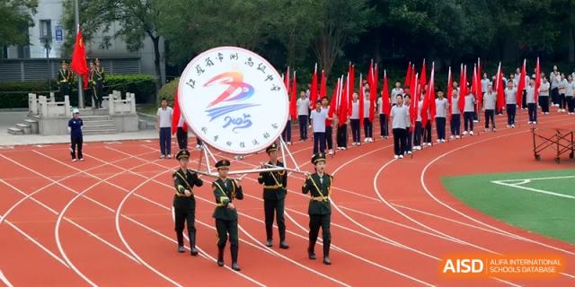 Students in ceremonial uniforms march with a large circular emblem on a red track at Changzhou Senior High School of Jiangsu Province.