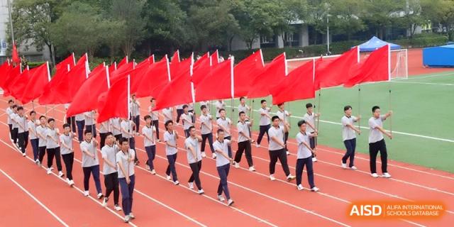 A formation of students carries large red flags across the athletic field during a parade at Changzhou Senior High School of Jiangsu Province.