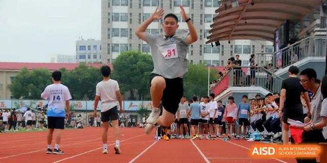 A male student athlete captured mid-air during a dynamic long jump attempt into the sand at Changzhou Senior High School of Jiangsu Province.