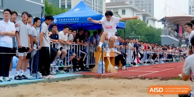 A student in a white jersey leaps into the air during a competitive long jump event at Changzhou Senior High School of Jiangsu Province.