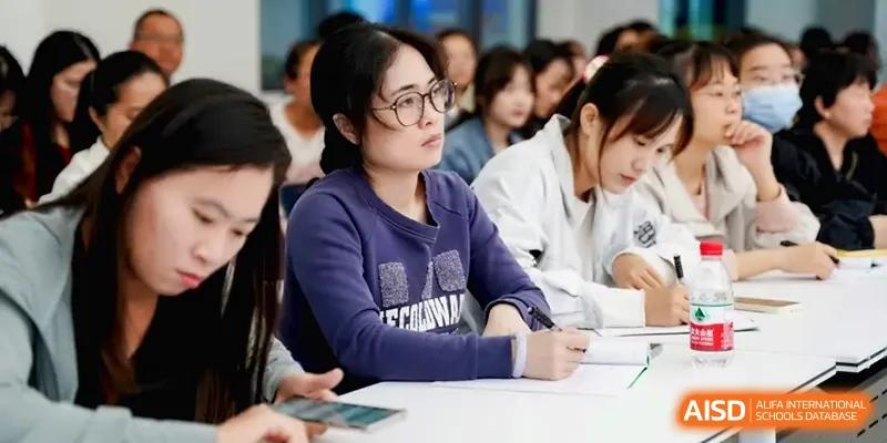 A young woman in a purple sweater takes diligent notes while attending an educational lecture at Beijing Haidian Foreign Language Shi Yan School Hainan Campus.