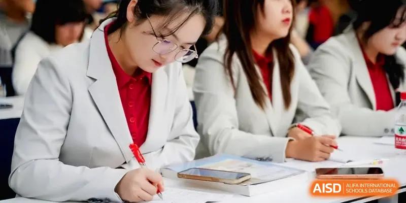 A student in a white blazer focuses on writing in her notebook during a lesson at the Beijing Haidian Foreign Language Shi Yan School Hainan Campus.