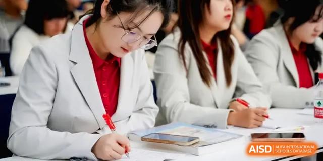 A student in a white blazer focuses on writing in her notebook during a lesson at the Beijing Haidian Foreign Language Shi Yan School Hainan Campus.