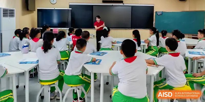 A teacher leads a group of students in green and white uniforms sitting at round tables at Beijing Haidian Foreign Language Shi Yan School Hainan Campus.