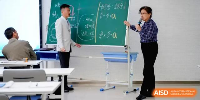 Two educators stand by a chalkboard covered in mathematical equations during a lecture at Beijing Haidian Foreign Language Shi Yan School Hainan Campus.