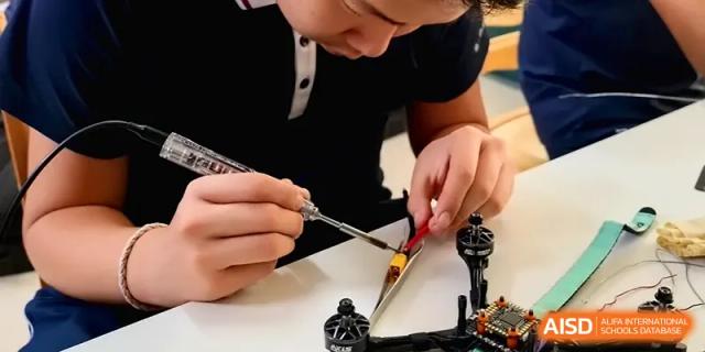 A student works with precision using a tool on a drone component in a technical workshop at Beijing Haidian Foreign Language Shi Yan School Hainan Campus.