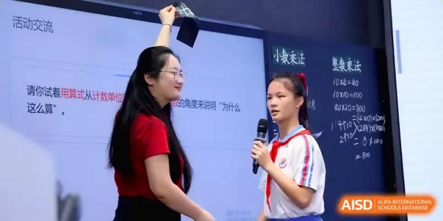 A teacher interacts with a student holding a microphone during a collaborative classroom session at Beijing Haidian Foreign Language Shi Yan School Hainan Campus.