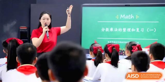 An educator gestures toward a digital presentation while teaching a group of attentive students at Beijing Haidian Foreign Language Shi Yan School Hainan Campus.