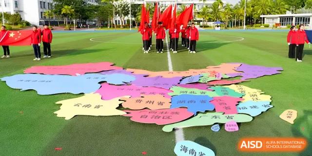 Students stand behind a large colorful map on a sports field during a cultural event at Beijing Haidian Foreign Language Shi Yan School Hainan Campus.