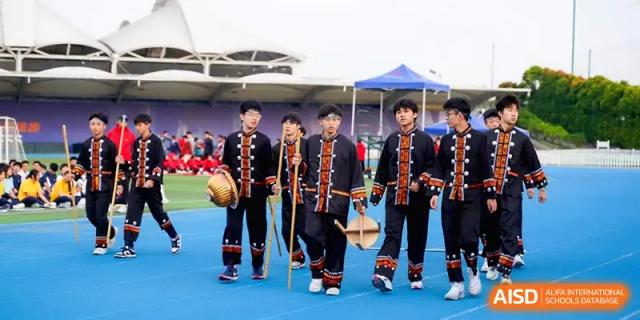 Students wearing traditional dark ethnic clothing walk in a procession during a festival at Beijing Haidian Foreign Language Shi Yan School Hainan Campus.