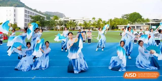 Several students in flowing blue costumes perform a synchronized dance outdoors at Beijing Haidian Foreign Language Shi Yan School Hainan Campus.