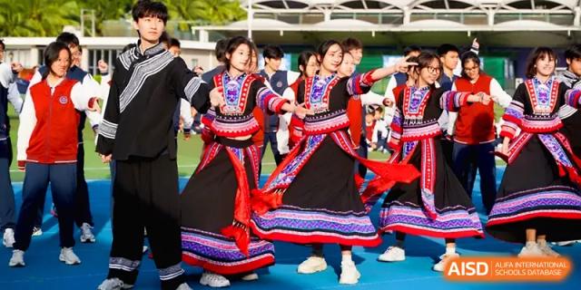 Performers in vibrant traditional dresses with red patterns dance during a celebration at Beijing Haidian Foreign Language Shi Yan School Hainan Campus.