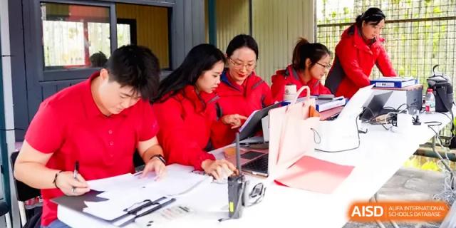 Three staff members in red shirts work together on a laptop during an outdoor school event at Beijing Haidian Foreign Language Shi Yan School Hainan Campus.