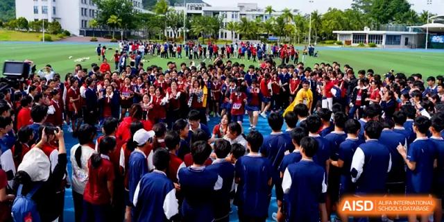 A large group of students in blue uniforms gathers on the blue sports field for a team activity at Beijing Haidian Foreign Language Shi Yan School Hainan Campus.
