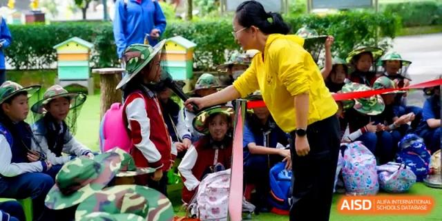 A teacher in a yellow shirt interacts with students during a hands-on outdoor learning activity at Beijing Haidian Foreign Language Shi Yan School Hainan Campus.
