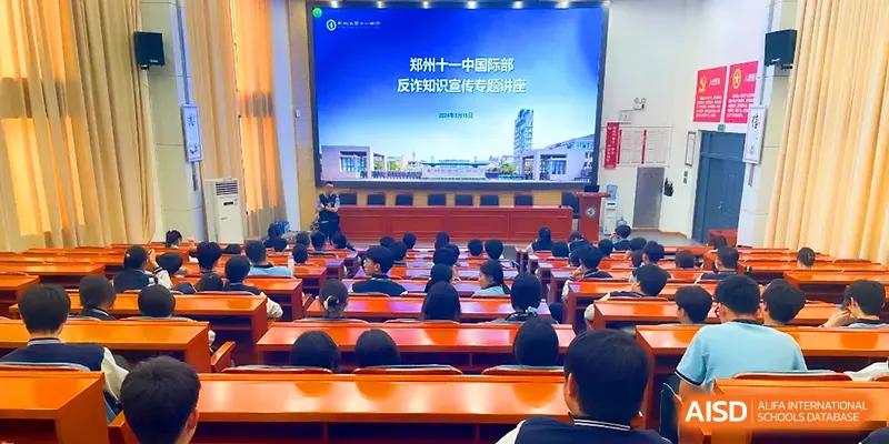 An auditorium view of a large screen displaying a presentation to a seated audience of students and staff at Zhengzhou No.11 High School.