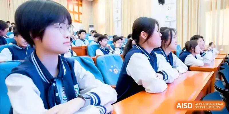 Students in school uniforms sit at orange desks in a lecture hall, listening attentively during a presentation at Zhengzhou No.11 High School.