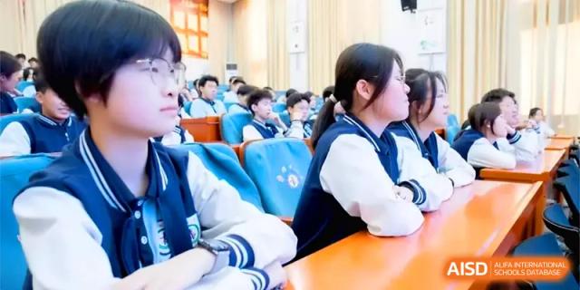 Students in school uniforms sit at orange desks in a lecture hall, listening attentively during a presentation at Zhengzhou No.11 High School.