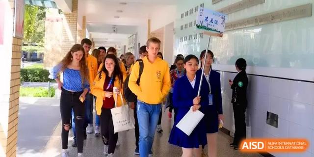 International and local students walk together through a bright school hallway, carrying bags and signs at Zhengzhou No.11 High School.